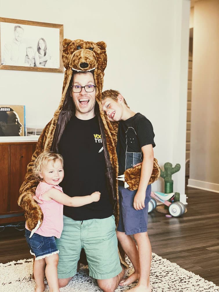 Schyler Manning in a bear costume while hugging two kids